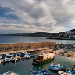 Boats in harbor against cloudy sky