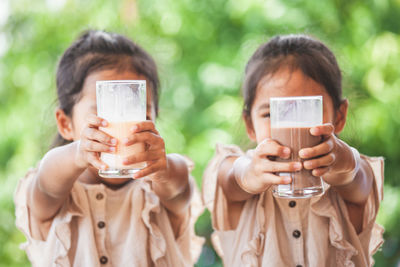 Friends holding drinking glasses against tree