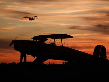 Silhouette propeller airplanes against orange sky during sunset