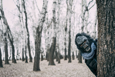 Portrait of man wearing mask while standing by tree during winter