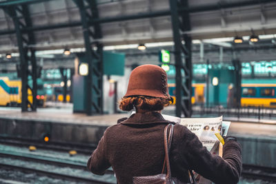 Woman reading newspaper while standing at railroad station platform