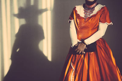 Midsection of woman in dress holding purse while standing against wall with shadow