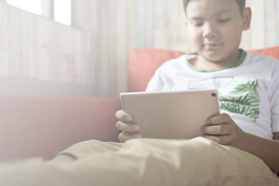 Close-up of boy using mobile phone while sitting on bed