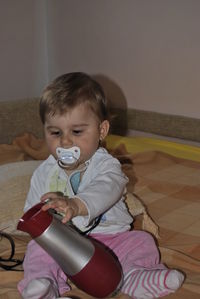 Cute boy holding hair dryer on bed at home