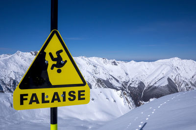 Information sign on snowcapped mountain against blue sky