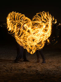 Fire dancers making heart shape on field at night