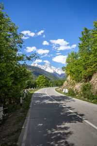 Empty road along trees and plants against sky