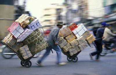 Side view of male workers carrying boxes on luggage carts at road