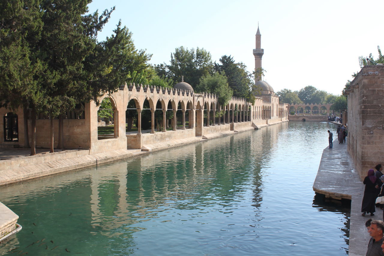 water, architecture, built structure, building exterior, tree, waterfront, reflection, canal, river, clear sky, day, lake, sky, incidental people, outdoors, nature, bridge - man made structure, connection, pier, rippled