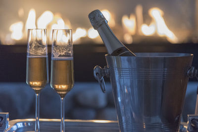 Champagne flutes by ice bucket against burning fireplace