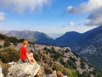 Rear view of woman sitting on mountain against sky