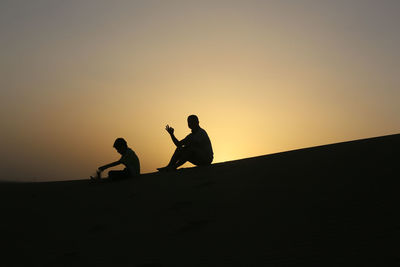 Silhouette of father and son sitting on sand
