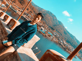 Young man sitting on shore against mountain