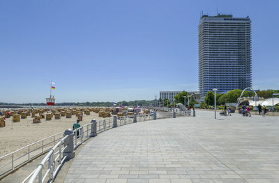 People on footpath by buildings against clear sky