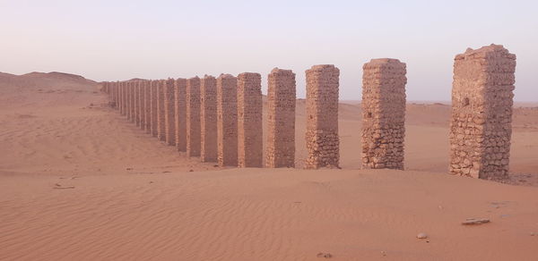 Wooden posts on sand against clear sky