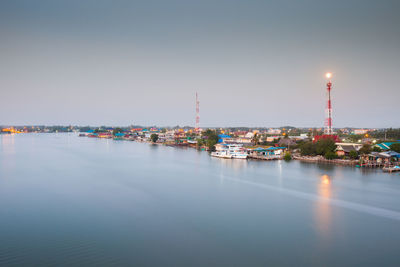 Illuminated buildings by sea against clear sky