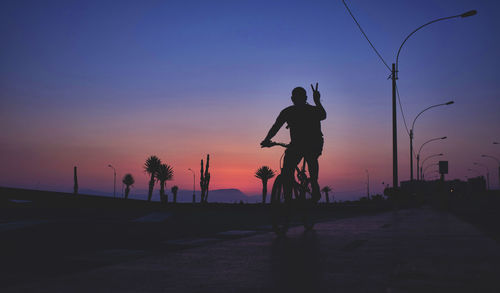 Silhouette man riding bicycle on road against sky during sunset