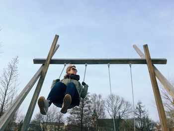 Low angle view of woman enjoying on swing against sky