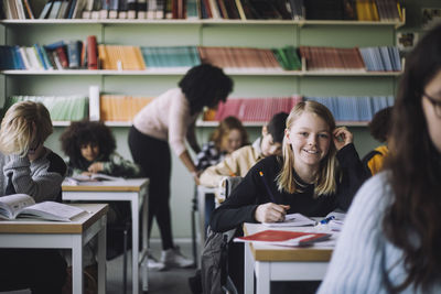 Portrait of smiling student sitting at desk in classroom