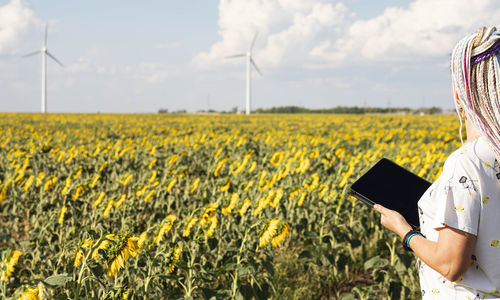 Young woman with tablet in field sunflowers, wind turbines for green energy, eco-energy, copy space