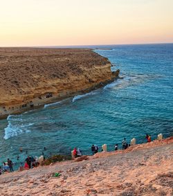 Group of people on rocks by sea against sky