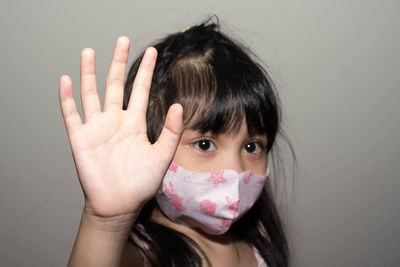 Cute girl gesturing while wearing mask against gray background