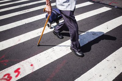 Low section of man crossing road holding a walking stick 