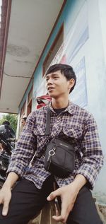 Full length of young man looking away while standing against wall