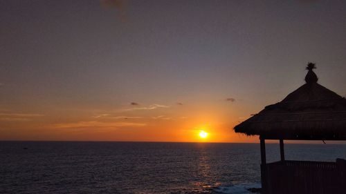 Silhouette built structure by sea against sky during sunset