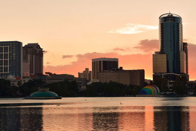 Sea by buildings against sky during sunset