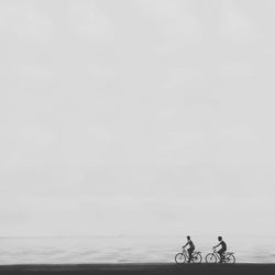 Men riding bicycle on beach against clear sky
