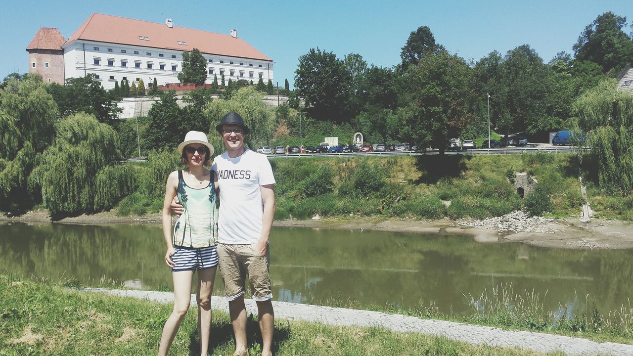 person, water, casual clothing, lifestyles, leisure activity, standing, tree, young adult, full length, building exterior, three quarter length, grass, built structure, young men, front view, architecture, smiling, looking at camera