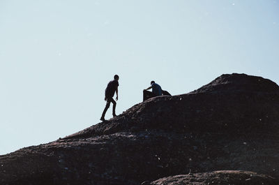 Low angle view of men on rock against sky