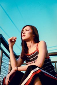 Low angle view of young woman looking away against blue sky