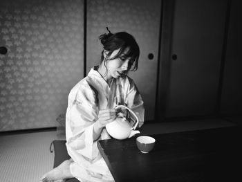 Woman holding cup while sitting on table at home