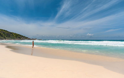 Woman standing alone on tropical sandy beach with idyllic turquoise ocean and waves