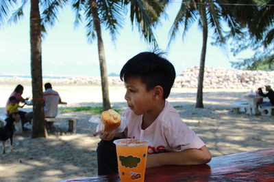 Boy eating food at beach against trees