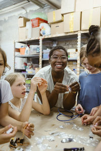 Portrait of smiling female teacher with students working with electrical components at workshop in school