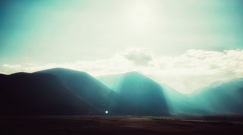 Sunlight streaming through mountain range against sky