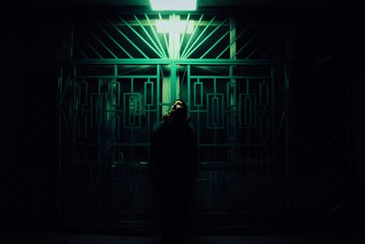 Thoughtful man standing by closed gate at night
