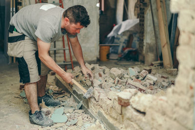 A young man breaks a brick wall with a sledgehammer.