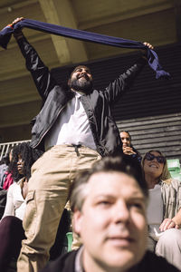 Low angle view of excited man cheering while holding sports scarf in stadium stand