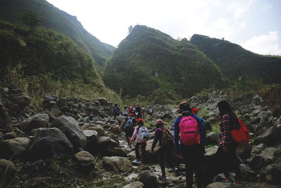 People standing on rocks by river against sky