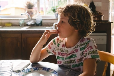 Child licks his fingers after eating something sweet, added film grain and background blur.