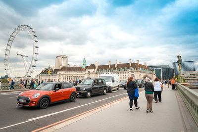 Cars on bridge by millennium wheel against sky in city