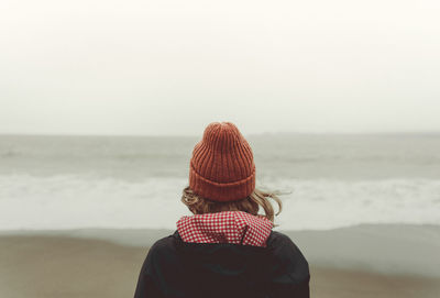 Rear view of woman wearing knit hat against sea at beach