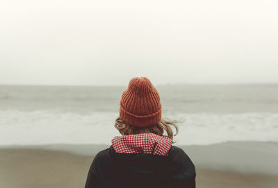 Rear view of woman standing at beach against clear sky