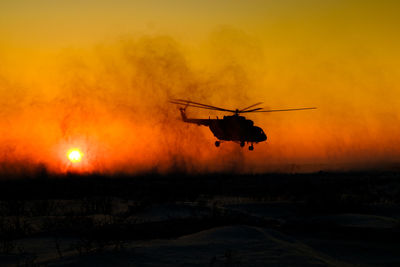 Silhouette airplane flying against sky during sunset