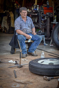 Full length of mechanic sitting on chair at garage