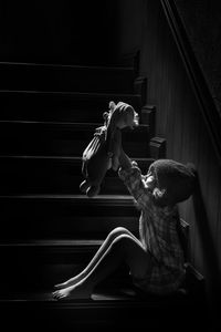 Cute girl holding stuffed toy sitting on staircase at home